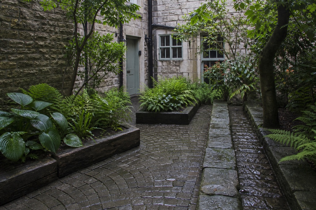 Small limestone courtyard with fan-laid setts, sleeper beds and a water rill