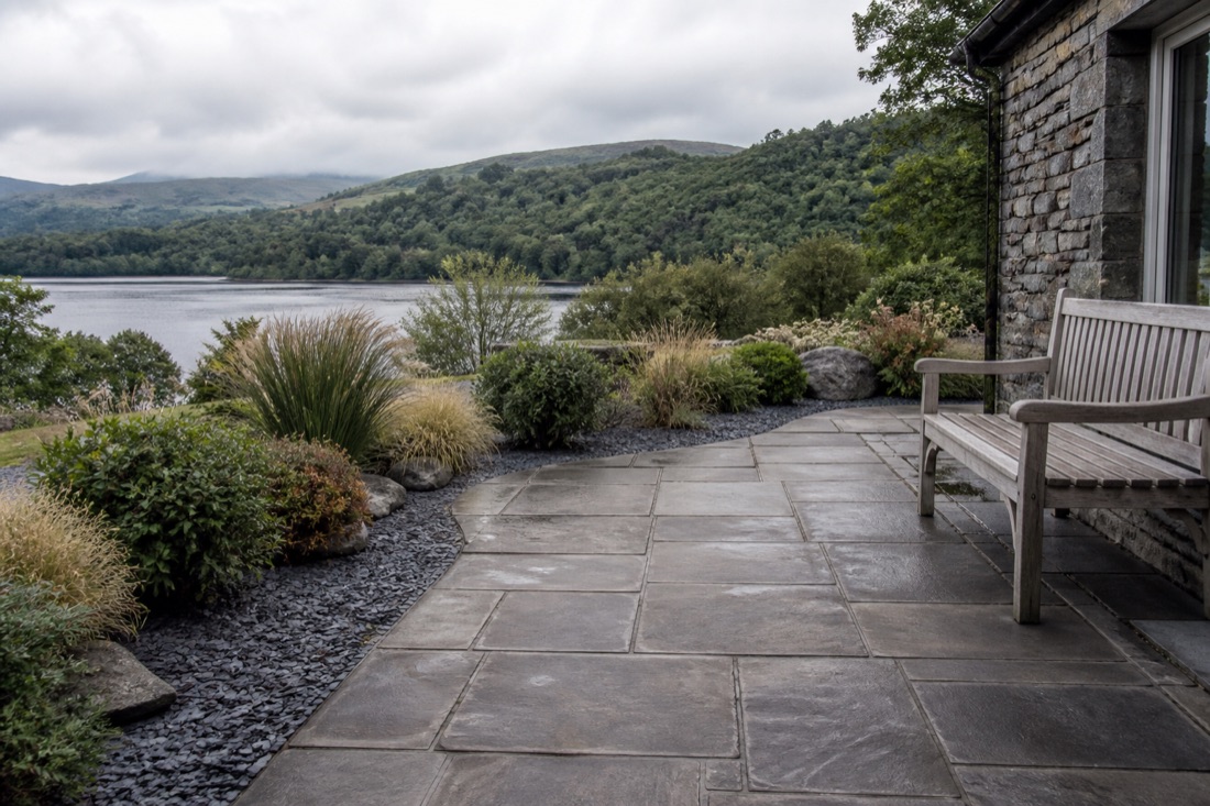 Sandstone terrace with a bench and low-maintenance planting overlooking a lake